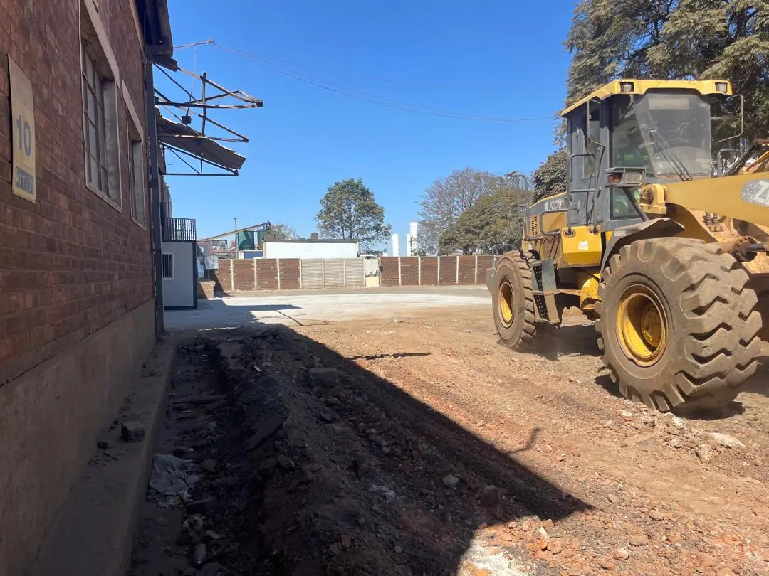 Earthmoving equipment preparing a construction site beside a brick building