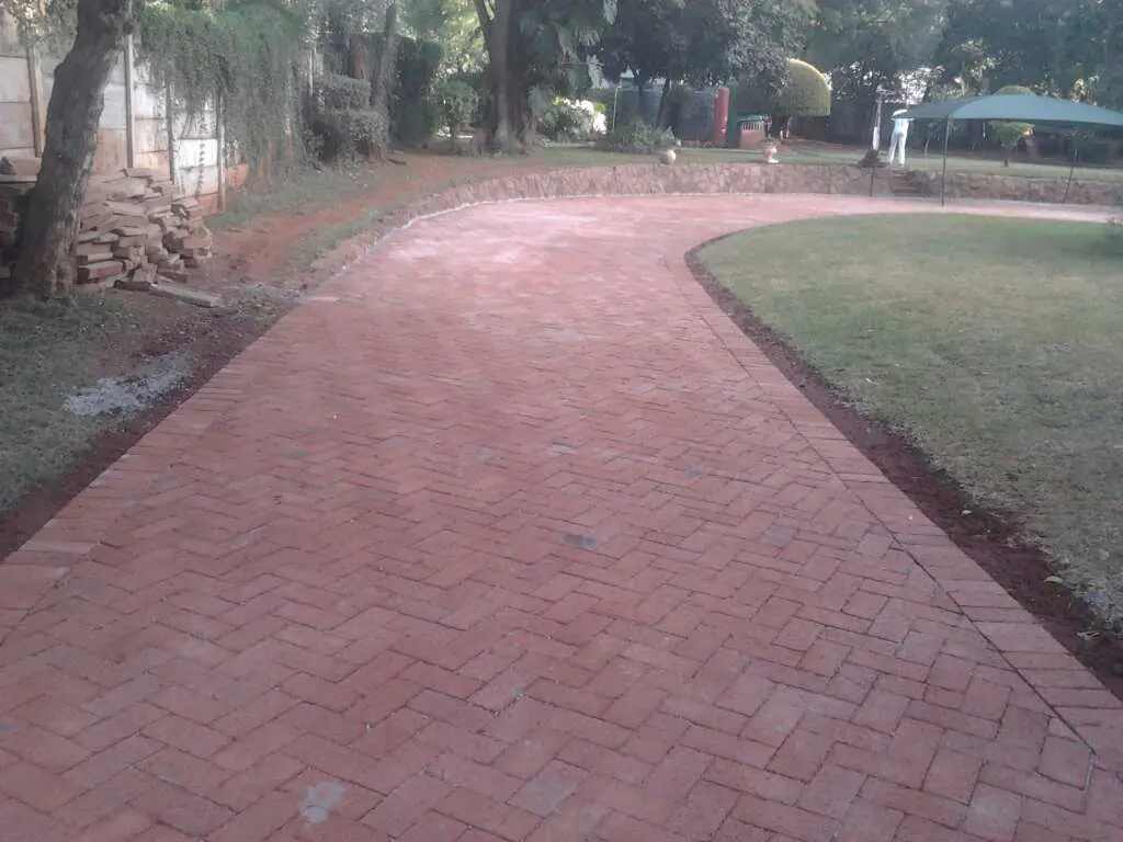 Red herringbone paved driveway curving beside a lawn